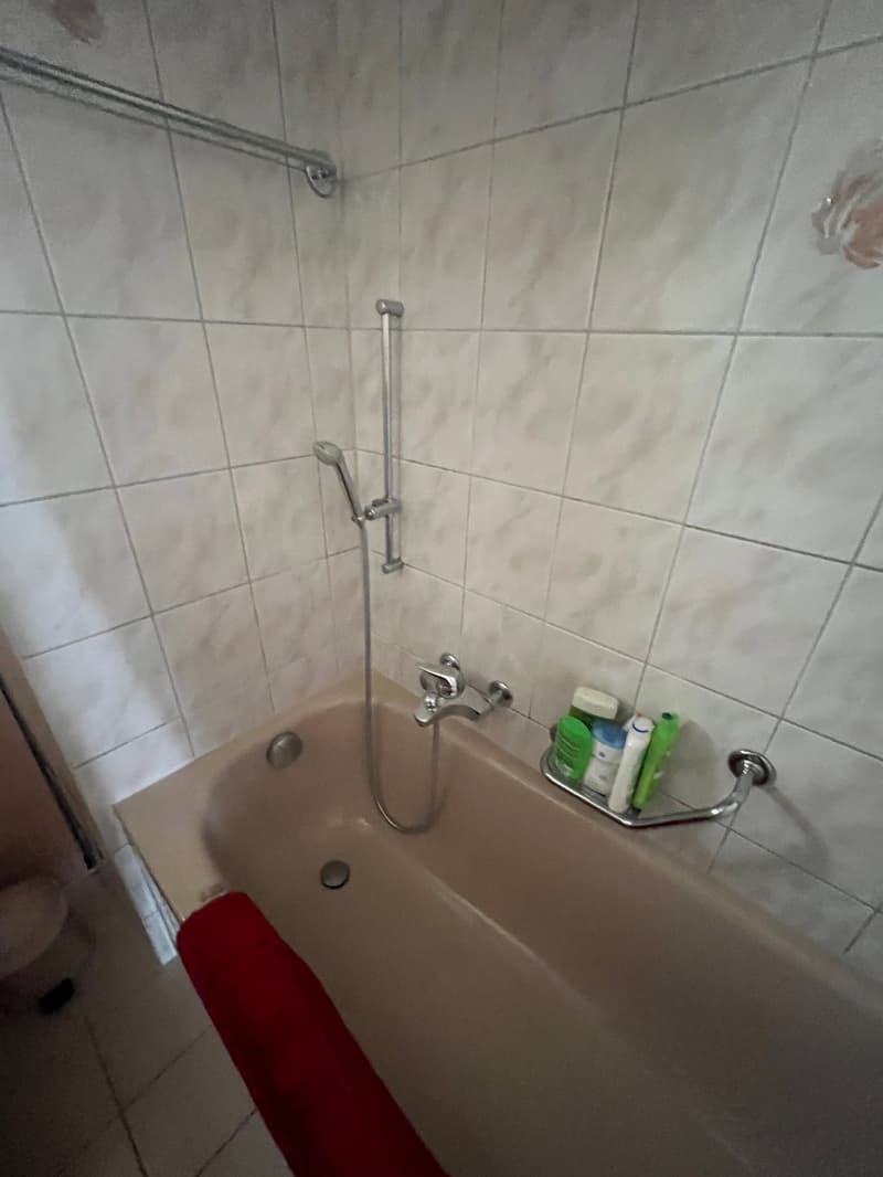 Bathtub with shower head, white tiles, red towel, toiletries on the wall
