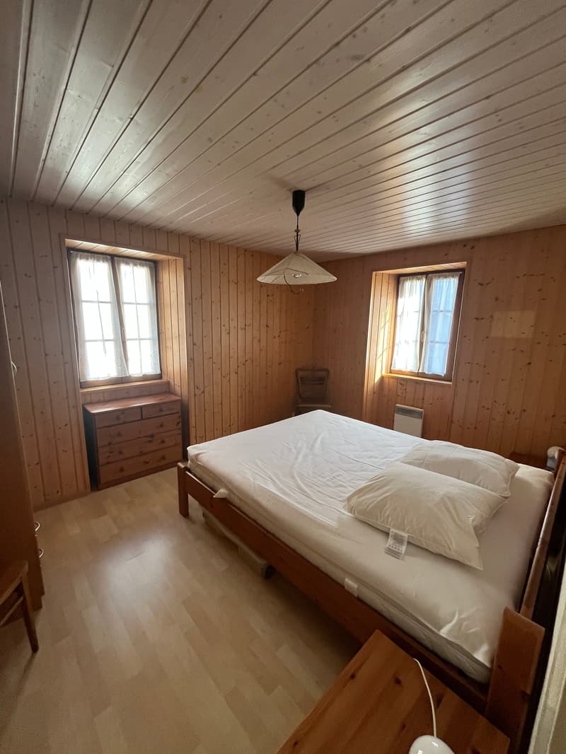 bedroom with wooden walls, bed, wooden cabinet, chair, windows, lamp