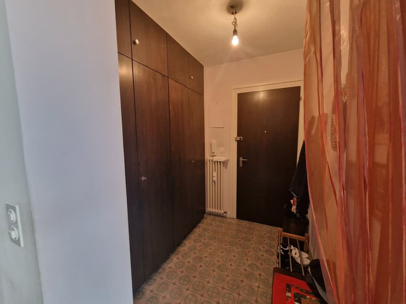 A hallway with wooden cabinets, tiled floor, a radiator, and a door.