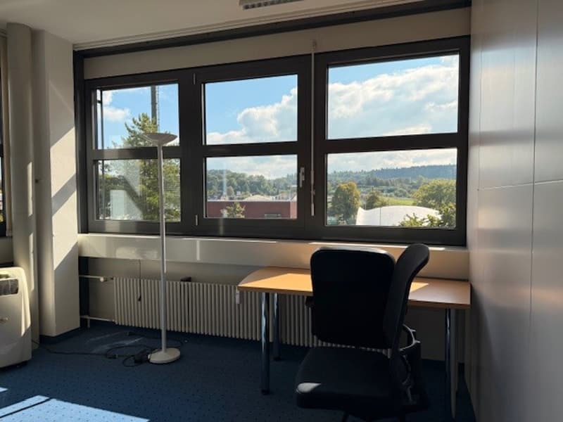Office room with desk, chair, radiator, floor lamp, and large windows with a view of the outside.