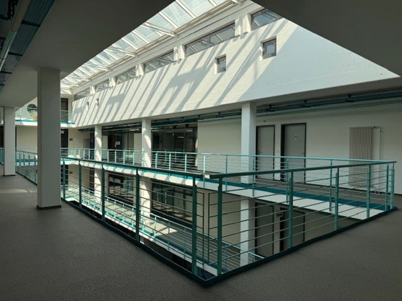 An empty building with a glass roof, metal railings, and a white wall