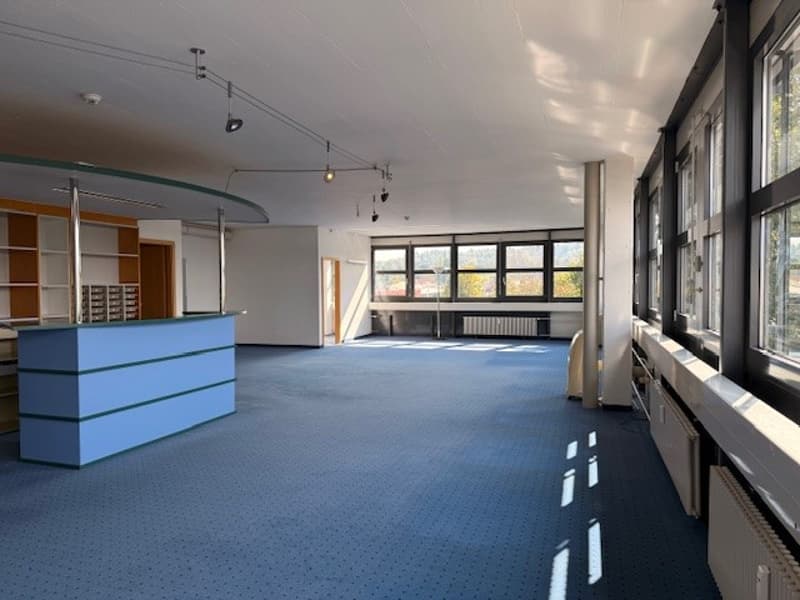 empty room, blue carpet, white walls, large windows, radiators, shelves, reception desk