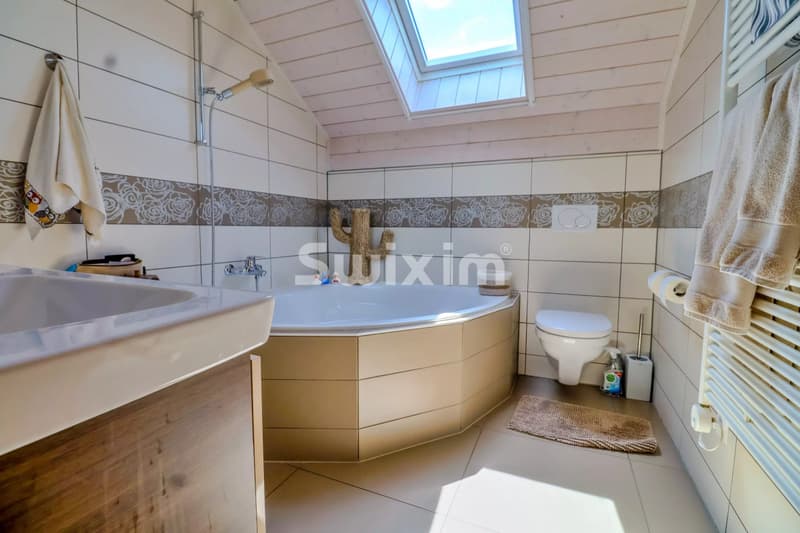 Salle de bain lumineuse avec baignoire et vue sur le ciel en pente.
