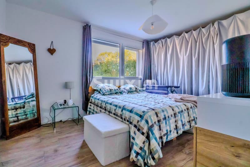 Chambre lumineuse avec vue sur le jardin, équipée d'un grand lit et de rideaux élégants.