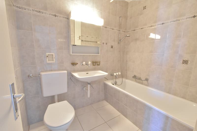 modern bathroom with white tiles, toilet, bathtub, sink, mirror
