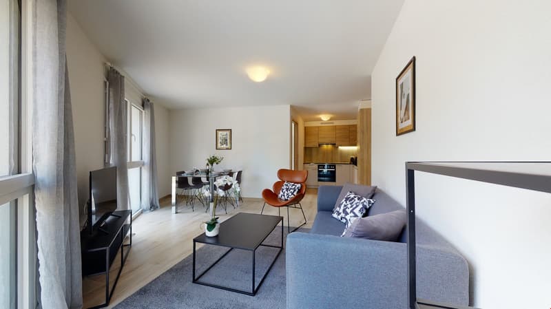 Blue couch, two armchairs, wooden floor, large window, television, table, table with flowers
