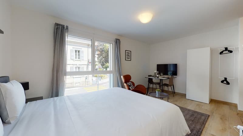 white bedding, desk with chair, TV, small rug, picture frame, window with curtains, lamp, storage cabinet