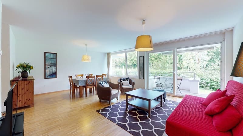 Dining room with wooden table, chairs, sofa, coffee table, rug, TV, picture frame, flower vase, hanging lamp, sliding door leading to balcony, outdoor seating, green plants