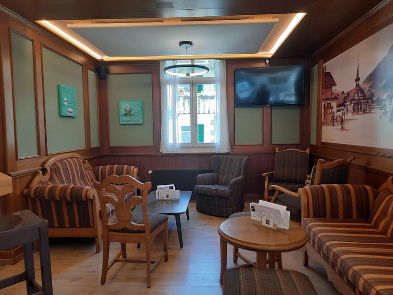 room with couches, wooden chairs, two tables, picture frames, a large window with a TV mounted above, a wall painting