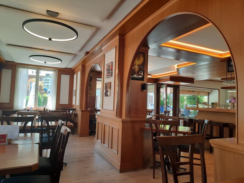 wooden floor, tables and chairs, large arched doorway, picture frames on the wall, large windows with white curtains, ceiling lamps
