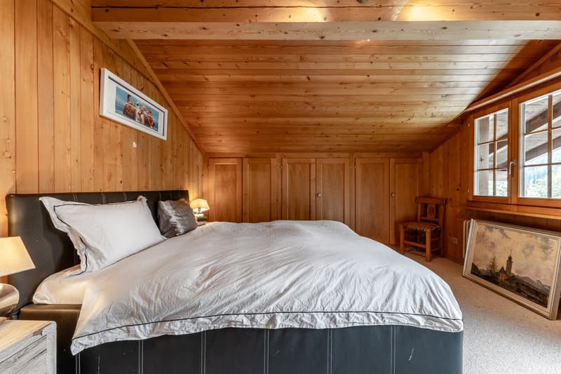 Bedroom: wooden walls, bed with white bedding, bedside lamps, wooden chair, paintings, wooden flooring