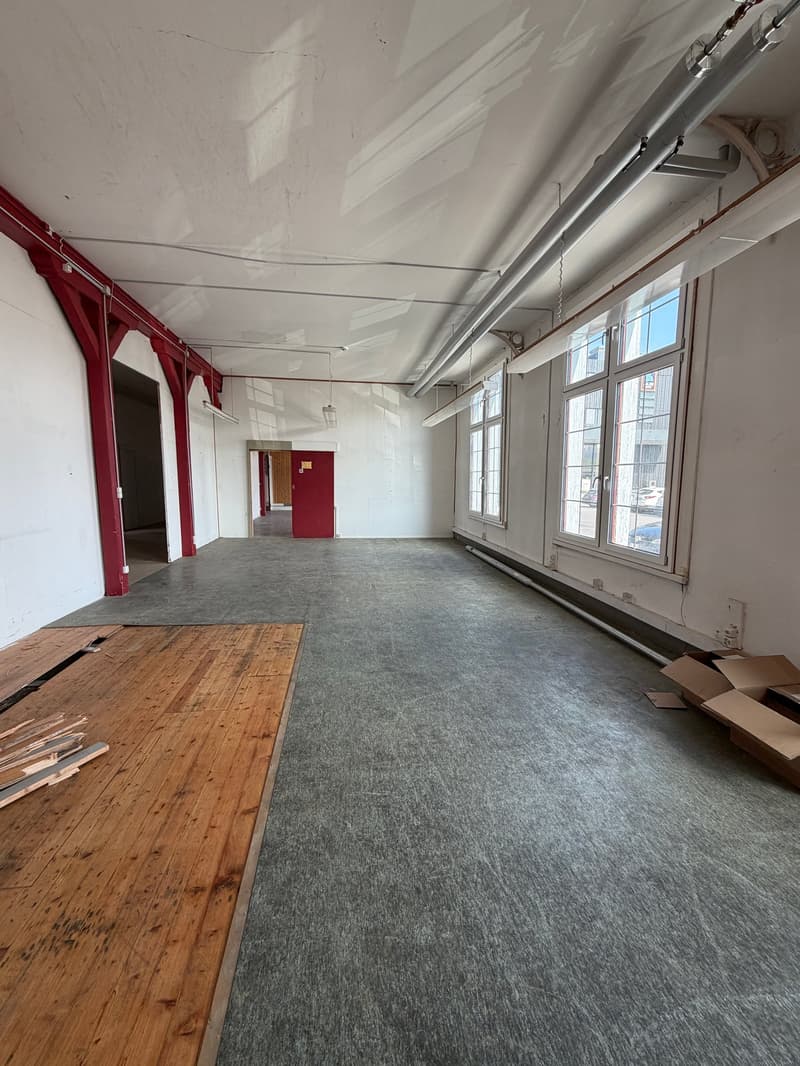 Empty room with wooden floor, gray carpet, red pillars, windows, and doors