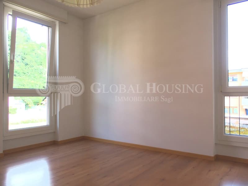 Empty room with hardwood floor, large windows, white walls, wooden trim