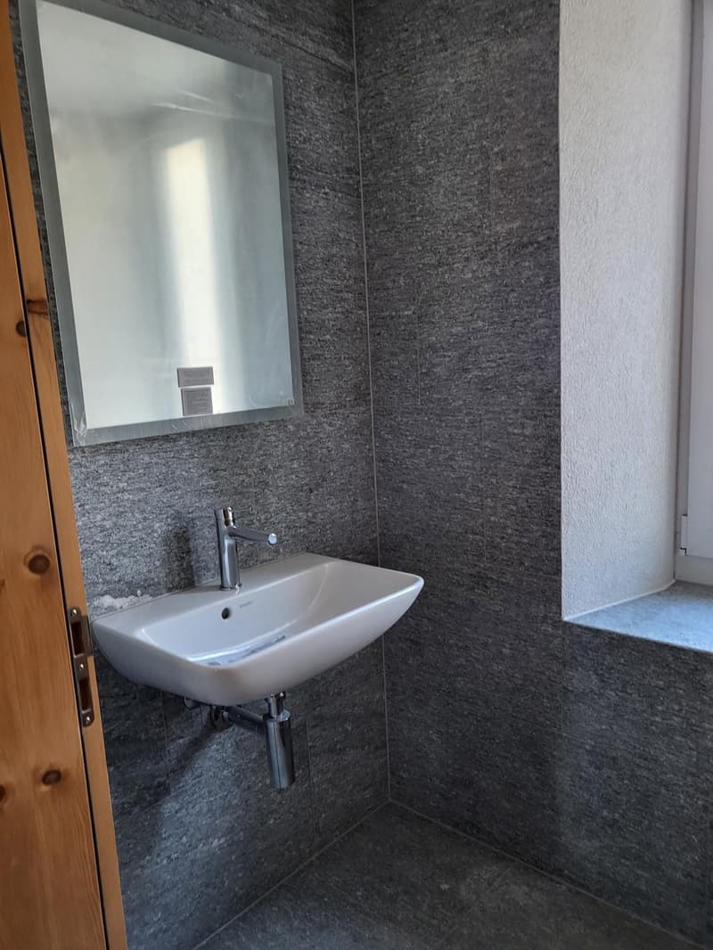 Gray textured walls, white porcelain sink, modern faucet, mirror mounted on wall
