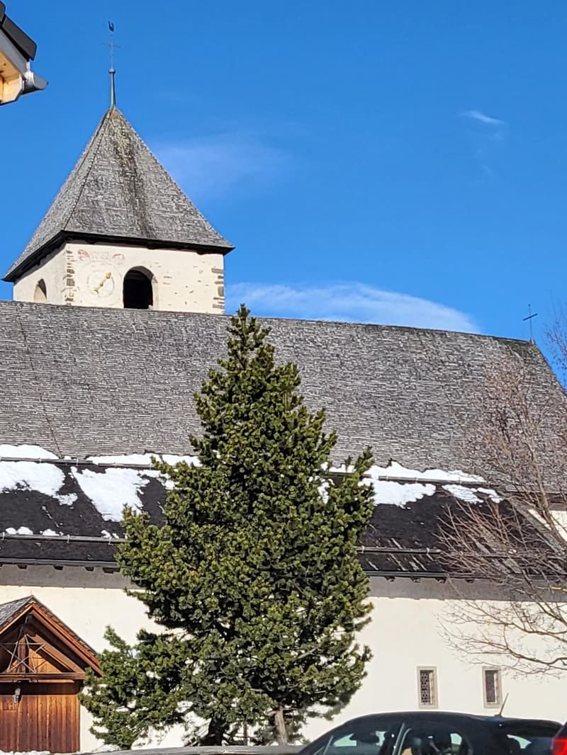 Church-style building with steeple, white and gray exterior, small windows, a small tree in front, snow on the roof