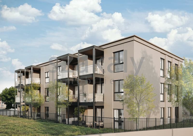 A modern multi-story apartment building with a beige exterior, large windows, and balconies. The building has a contemporary architectural design with clean lines and a mix of materials. It is surrounded by landscaping and fencing, creating a residential