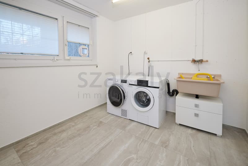 Laundry room with white tile floor, washing machine, dryer, sink, white walls, and a window with blinds