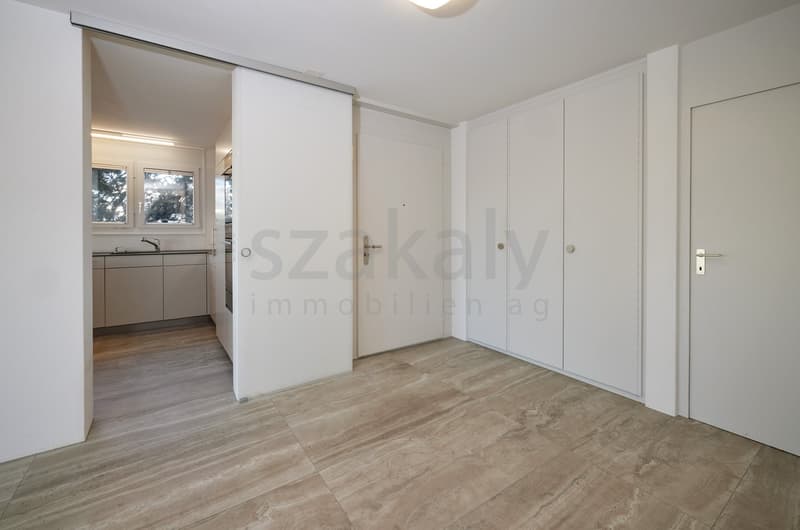 Empty room with sliding doors, modern design, tiled floor, light colored cabinets, kitchen with sink and faucet.