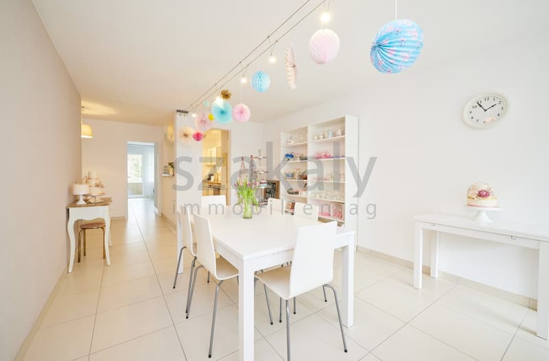 Dining room with white table and chairs, white walls, white tiled floor, white shelves, decorative items, and a clock on the wall.