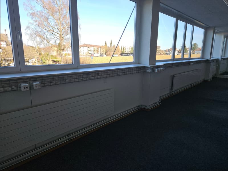 large windows, white walls, dark grey carpet, power outlets, white pipes