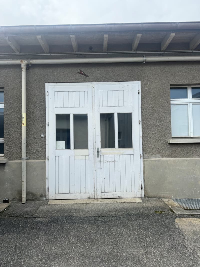Building facade with large white double doors, two windows, grey walls