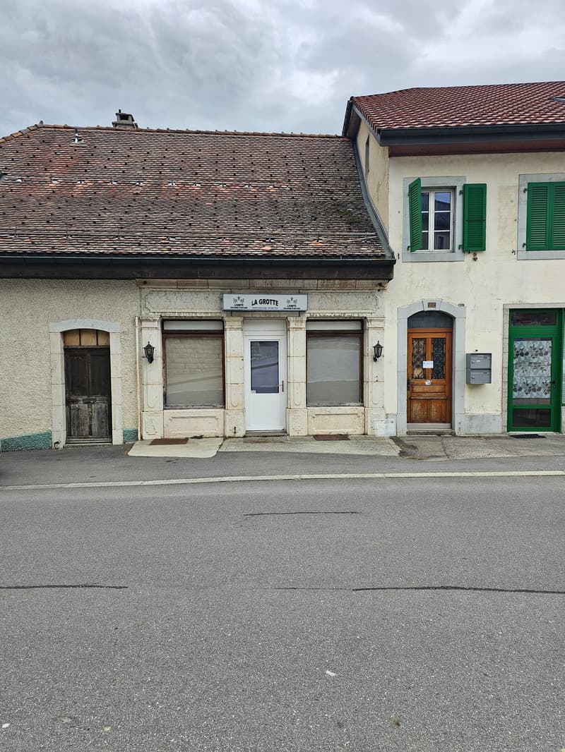 Building with a flat roof, wooden door, white door, windows with green shutters, wall lamp