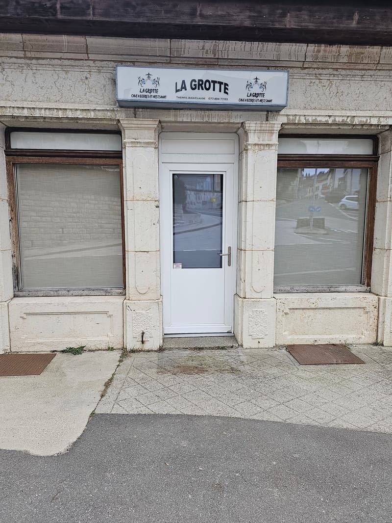 Old building with white door, glass windows, metal drain in front, signboard with 'LA GROTTE' on top