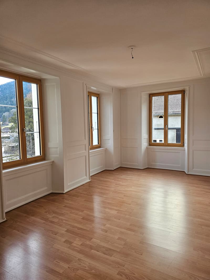 Spacious room with white walls, wooden floor, three large windows