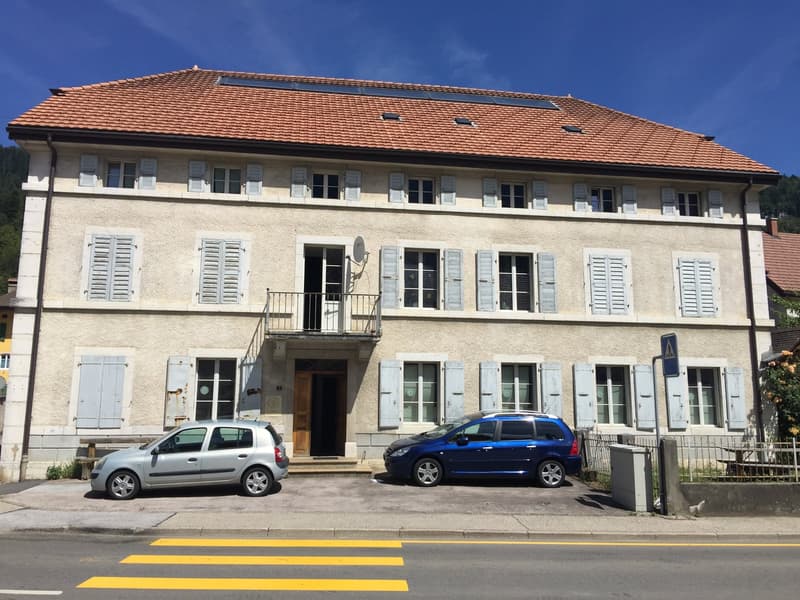 4 story building, multiple windows, solar panels on the roof, balconies in front of some windows, cars parked in front