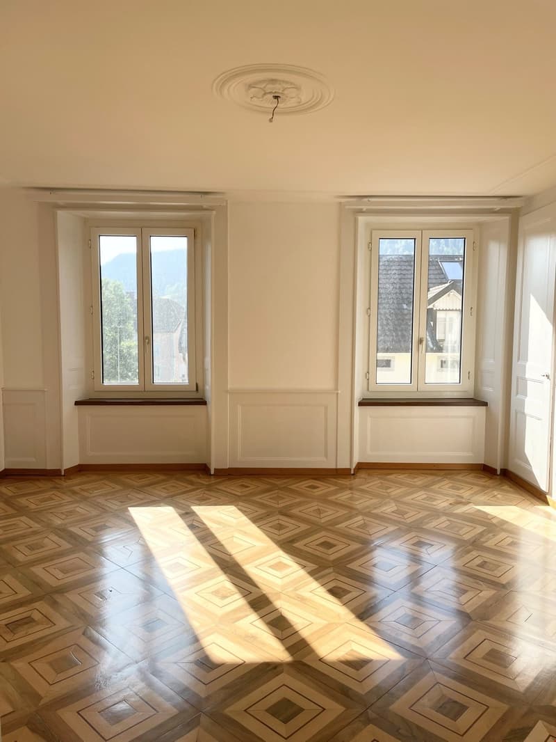 Empty room with parquet flooring, large windows, white walls, decorative ceiling