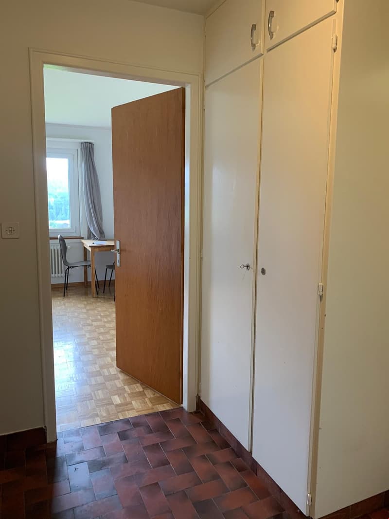 Empty room with wooden door, white wardrobes, wooden floor, desk, chair, window with curtains