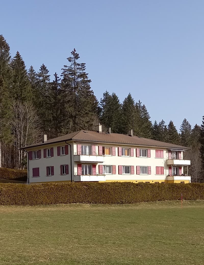 2 story house, white exterior, red shutters, brown roof, multiple balconies, surrounded by trees and grass