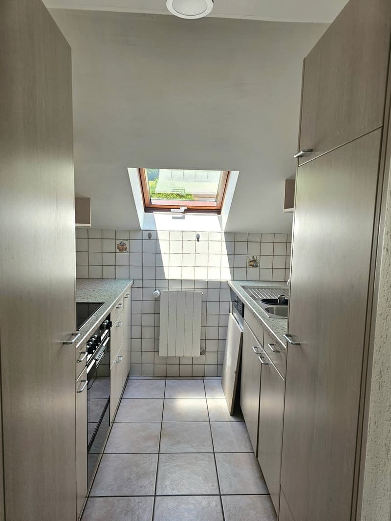 Galley-style kitchen with tiled floors, white cabinets, and a skylight window. The kitchen appears to have a dishwasher installed.