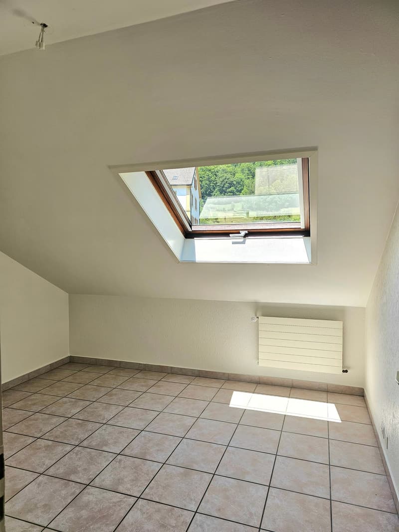 Spacious room with tile flooring, white walls, and a large skylight window providing natural light. The room appears to be a bedroom or living space with a radiator installed on the wall.