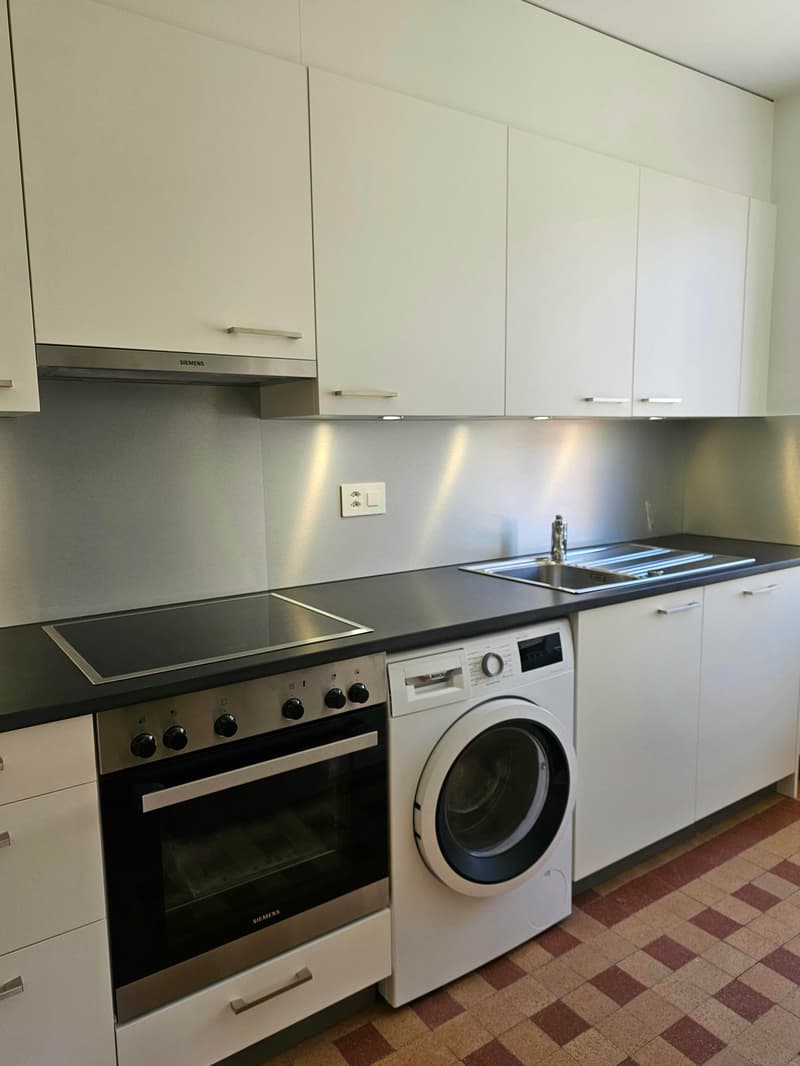 modern kitchen with white cabinets, black countertops, stainless steel appliances, including a stove, oven, and dishwasher, a white washing machine, and a sink with a faucet