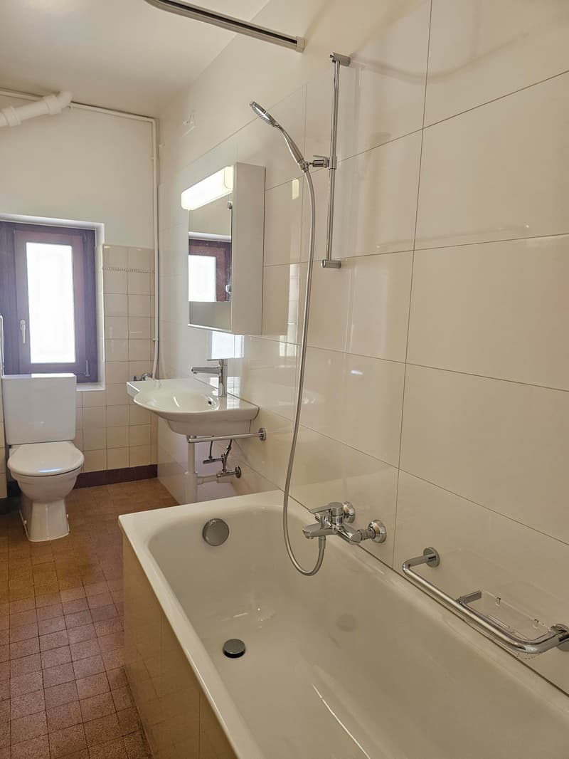 Bathroom with white tiles, bathtub, sink, toilet, shower head, mirror, window