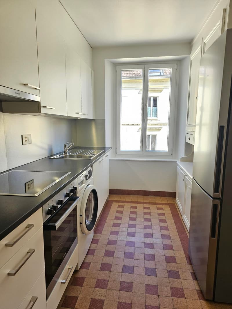 modern kitchen with white cabinets, black countertop, stainless steel appliances, washing machine, oven, sink, window