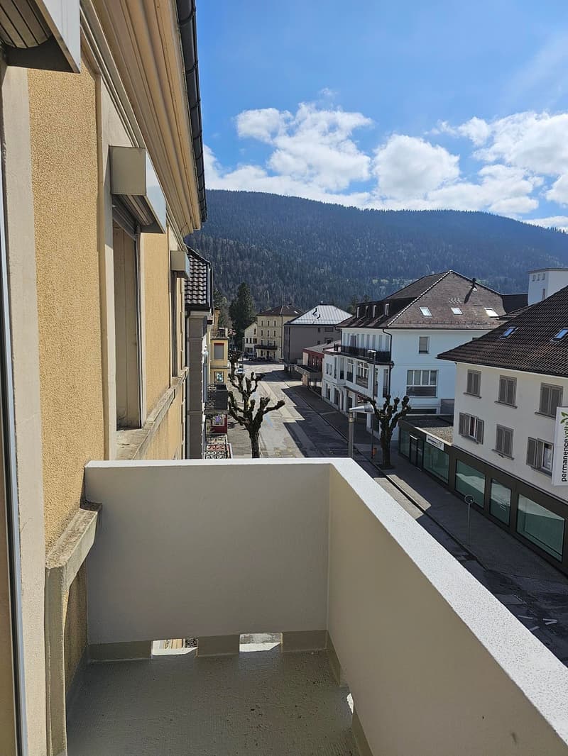 Balcony with railing, view of a street with buildings and mountains in the background