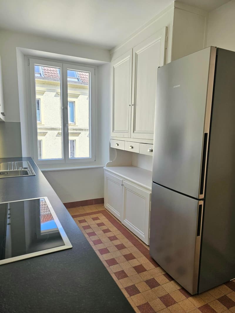 modern kitchen with white cabinets, stainless steel refrigerator, black countertop, double sink, tiled floor