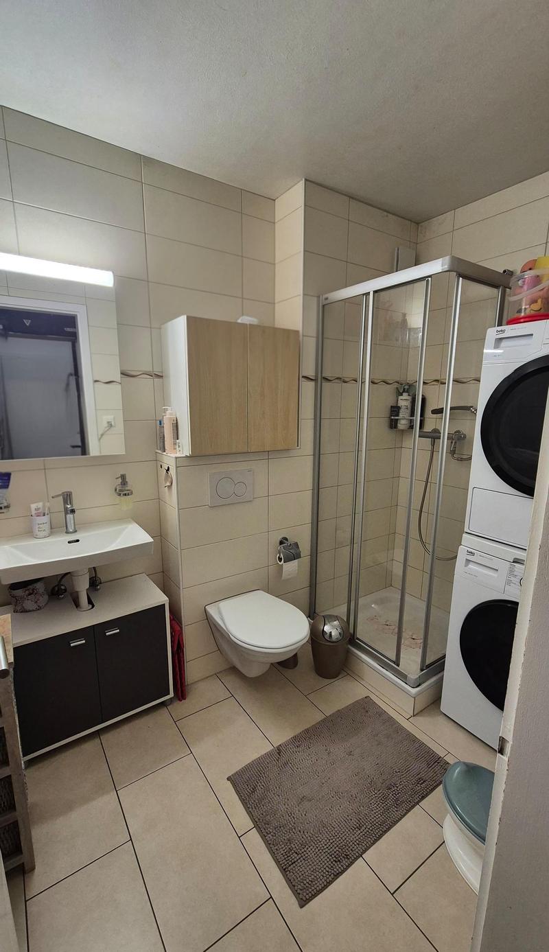 Bathroom with sink, toilet, shower, washing machine, and cabinet