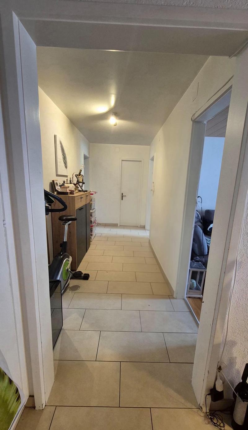 tiled floor, white walls, exercise bike, wooden cabinet, picture frame, lamp, door, couch, table