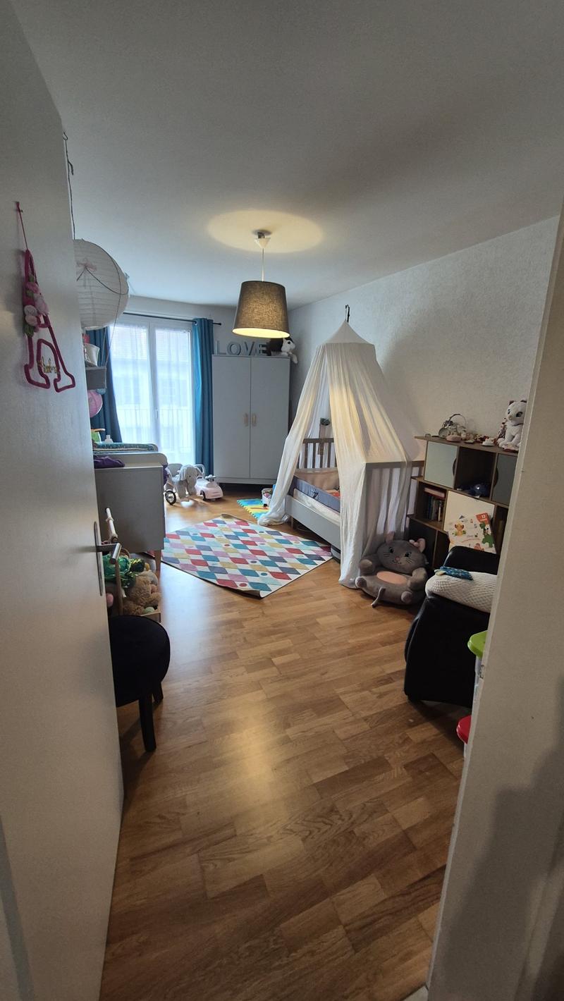 Wooden floor, white walls, bed with canopy, rug, toys, cabinet, window with blue curtains