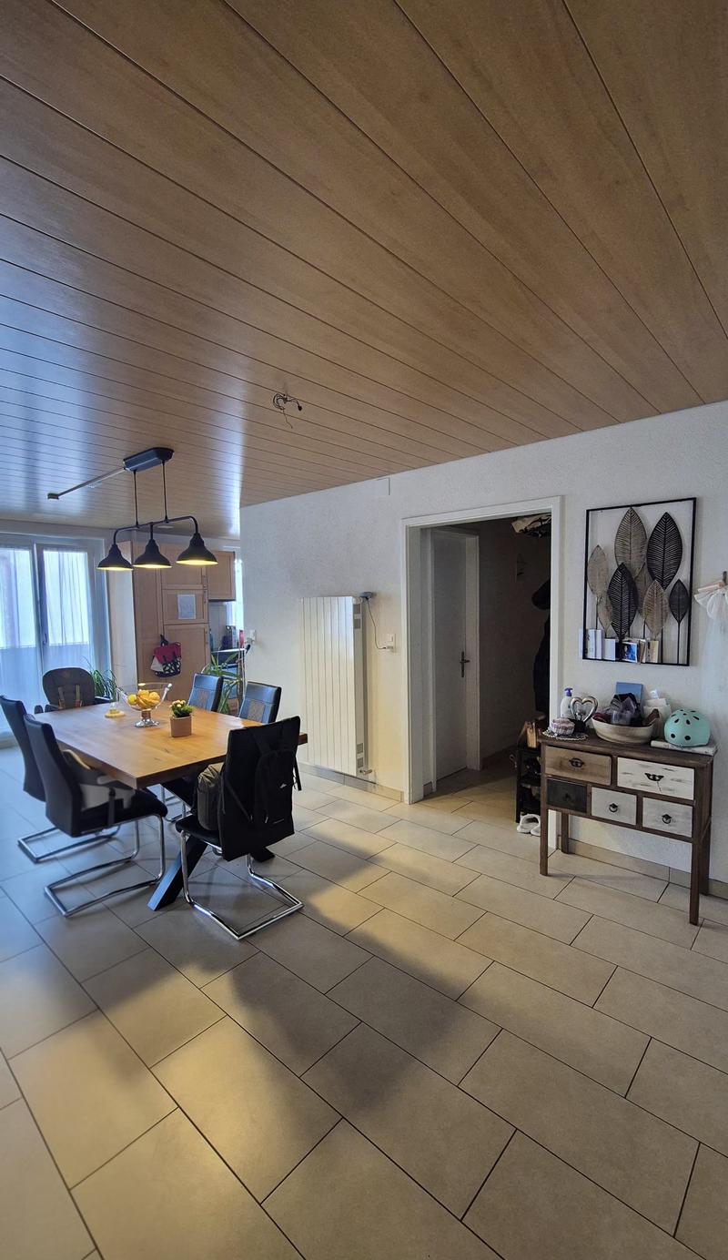 Dining room with wooden table, chairs, wooden cabinet, tiled floor, white walls, ceiling lights, radiator, and a framed picture on the wall.