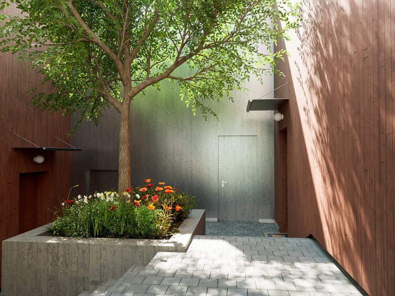 A small garden with a tree, flowers, and a concrete planter, surrounded by wooden walls and a brick floor.