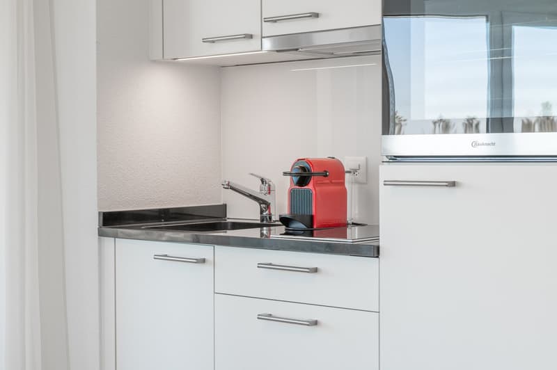 White cabinets, stainless steel countertop, silver faucet, coffee machine, microwave