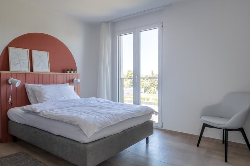 bedroom with bed, white sheets, white pillows, chair, glass doors, lamps, framed artworks, floored with wood