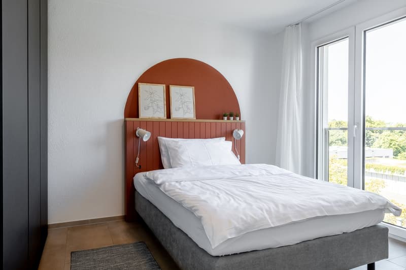 bed with white comforter, white pillows, nightstands with lamps, wooden headboard with two picture frames, rug, large windows