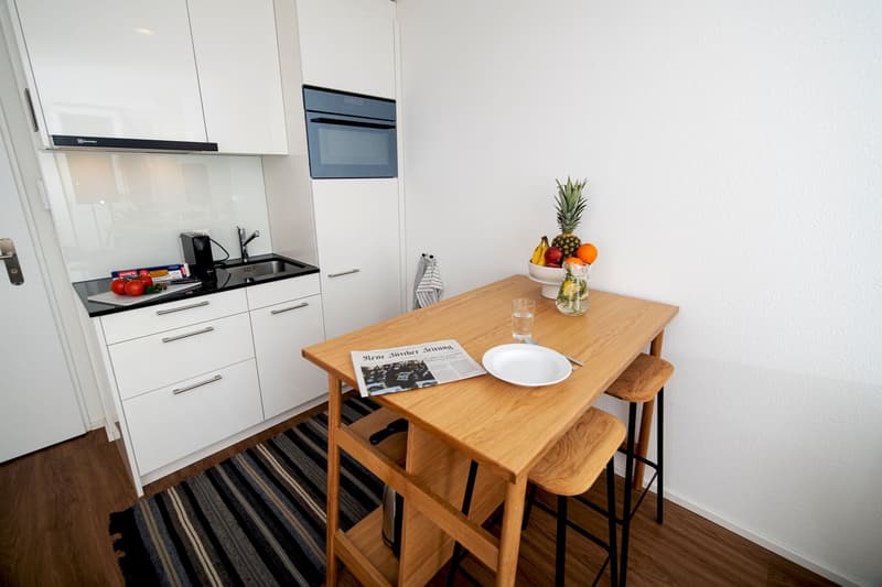 modern kitchen, wooden table, white cabinets, microwave, sink, dish cabinet, coffee maker, plate on table, bowl of fruits, plate on counter