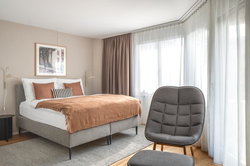 bedroom with bed, bedside tables, picture frame, curtains, chair, ottoman, carpet
