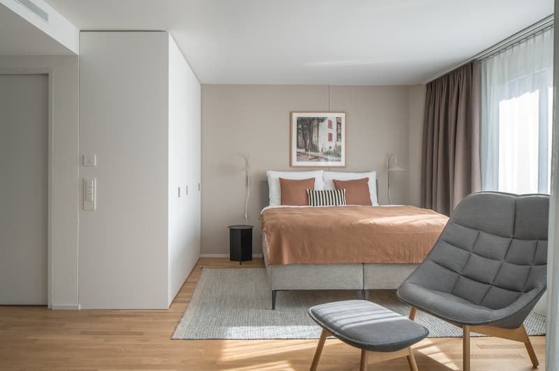 double bed with pillows, rug, chair, nightstand, lamps, beige wall, picture frame, window, white ceiling